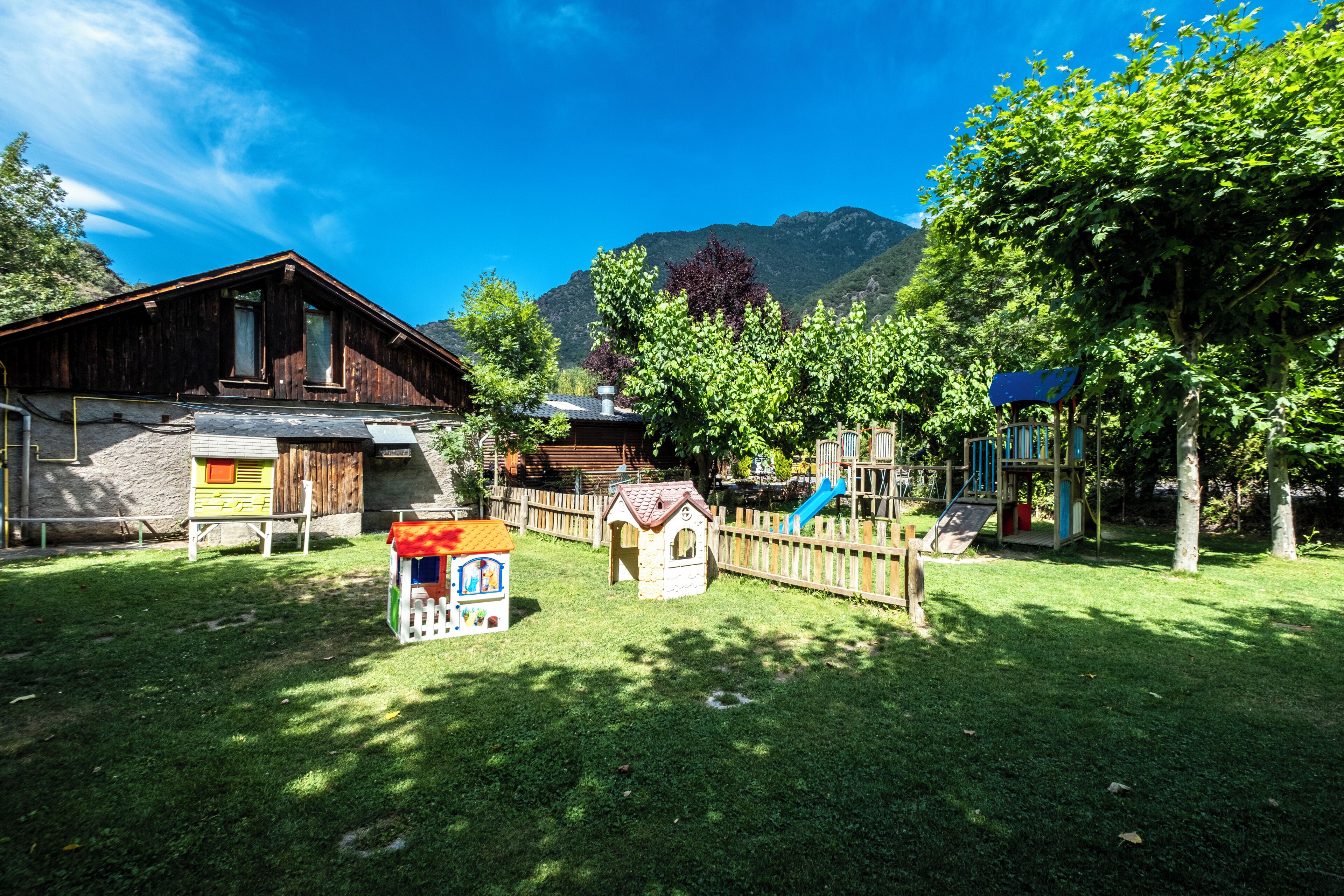 Una cabaña rústica de madera con base de piedra, una casita de juegos y un parque infantil con un tobogán.