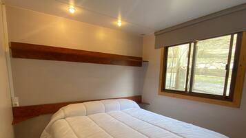 A bedroom with a bed, wooden headboard, a window with a view, and recessed ceiling lights.