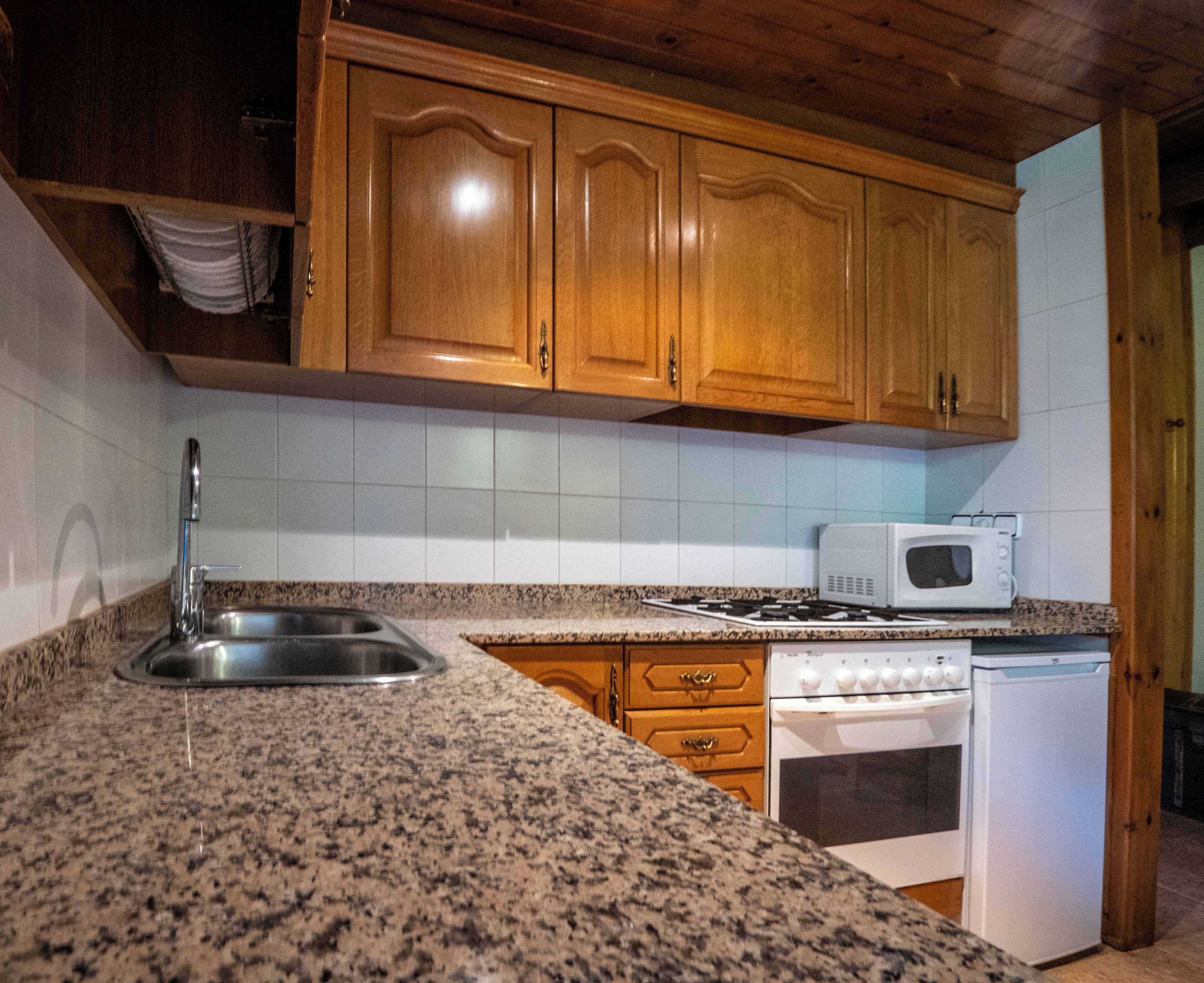 Een keuken met granieten aanrechtbladen, houten kastjes, een roestvrijstalen spoelbak, een magnetron, een fornuis en een vaatwasser.