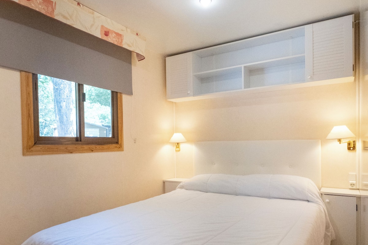 Un dormitorio con cama, lámparas de noche, una ventana y una estantería empotrada sobre la cama.