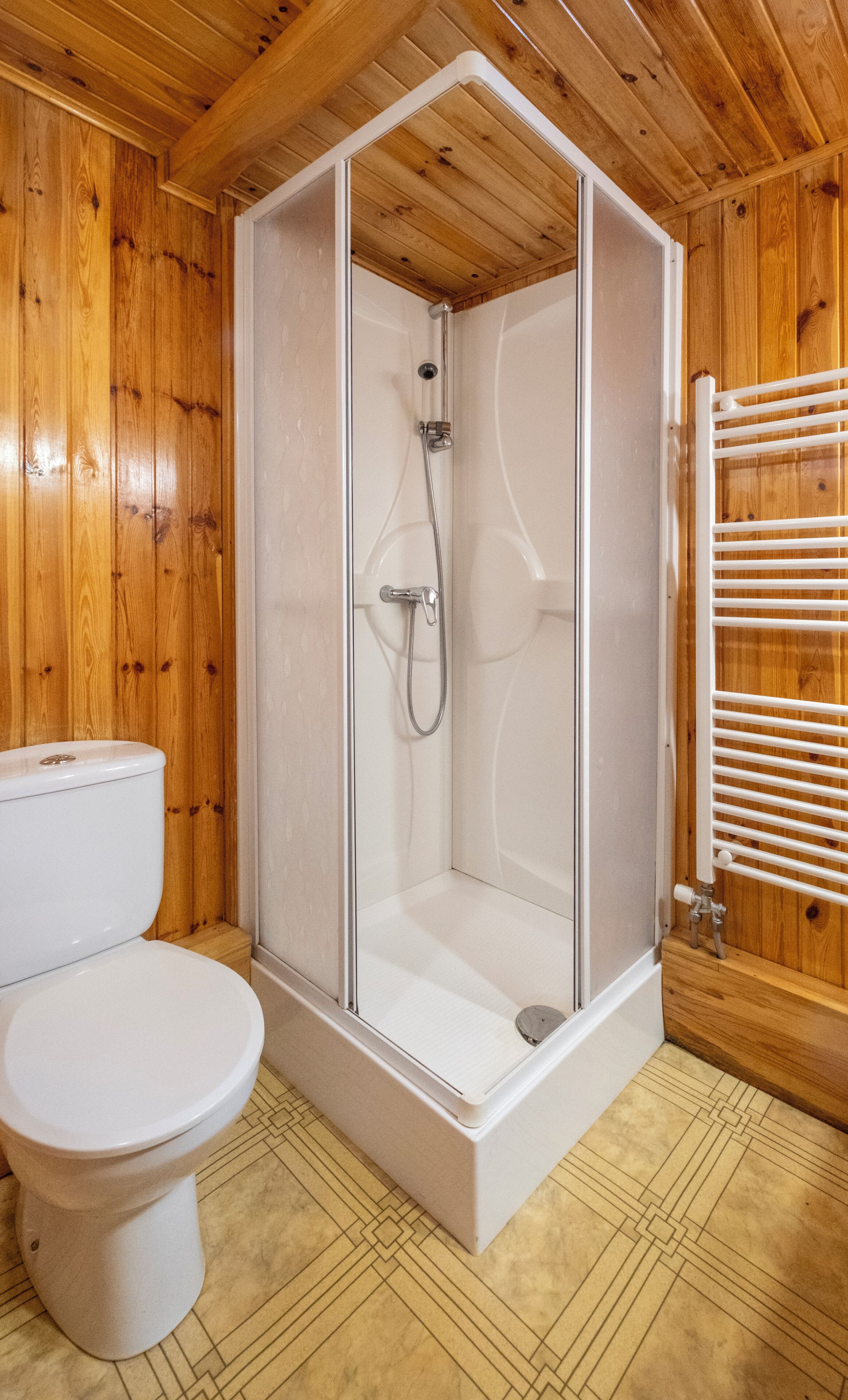 A wooden-paneled bathroom with a glass-enclosed shower, a toilet, and a towel rack.