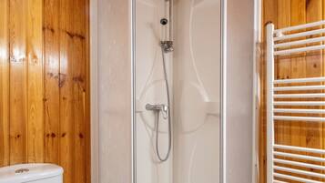 A wooden-paneled bathroom with a glass-enclosed shower, a toilet, and a towel rack.