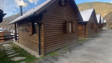 A row of wooden cabins with pitched roofs, a gravel driveway, and a mountain backdrop.