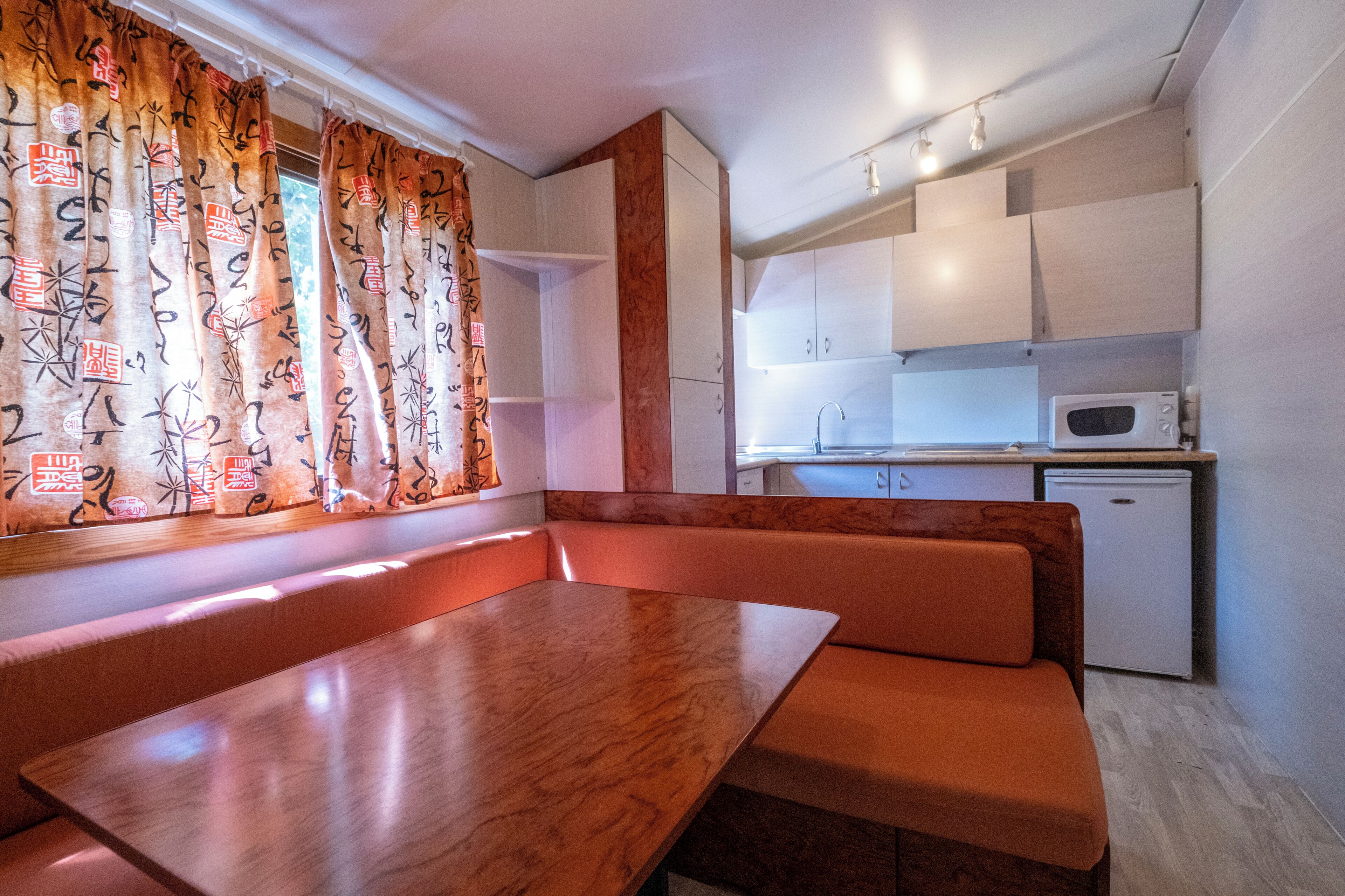 A compact kitchen with a microwave, a small refrigerator, and a wooden table with benches.