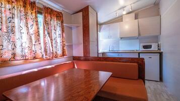 A compact kitchen with a microwave, a small refrigerator, and a wooden table with benches.