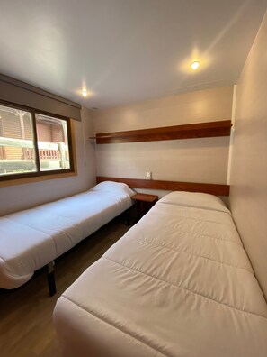 Una habitación con dos camas individuales, cabecero de madera, ventana con vistas y una lámpara en el techo.