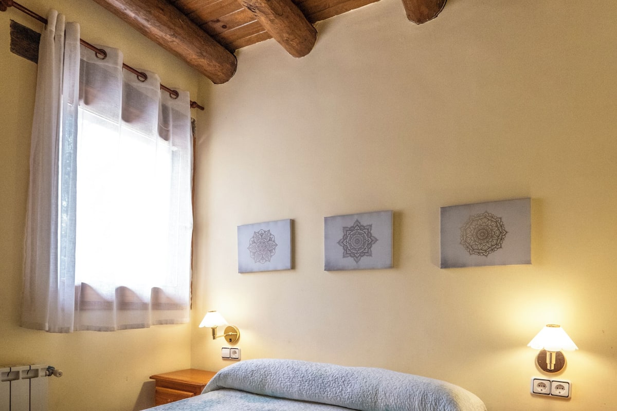 Un dormitorio con cama, mesita de noche, lámpara, ventana con cortinas y decoración en la pared.
