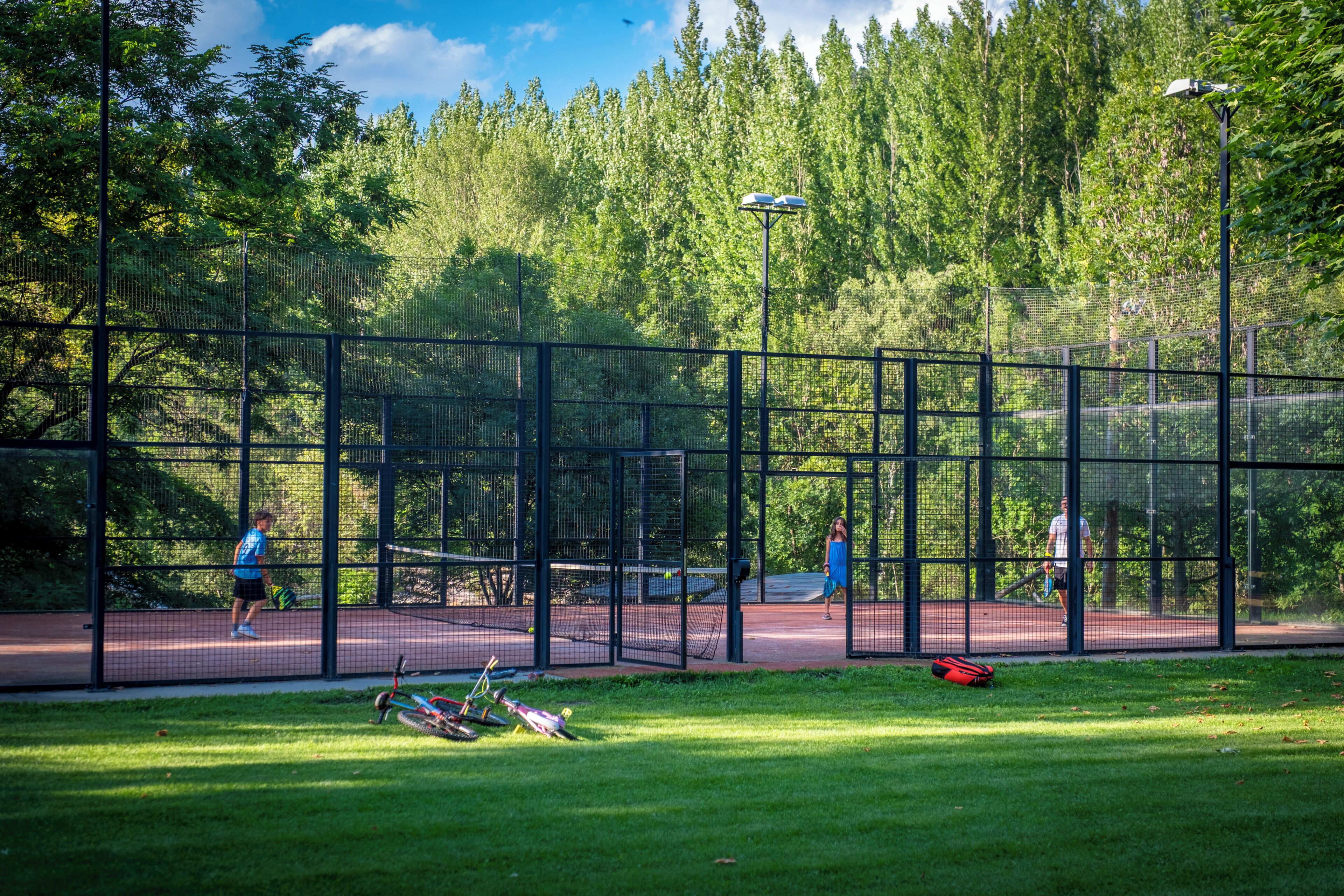 Un court de tennis en plein air, entouré d’une clôture, avec des arbres en arrière-plan.