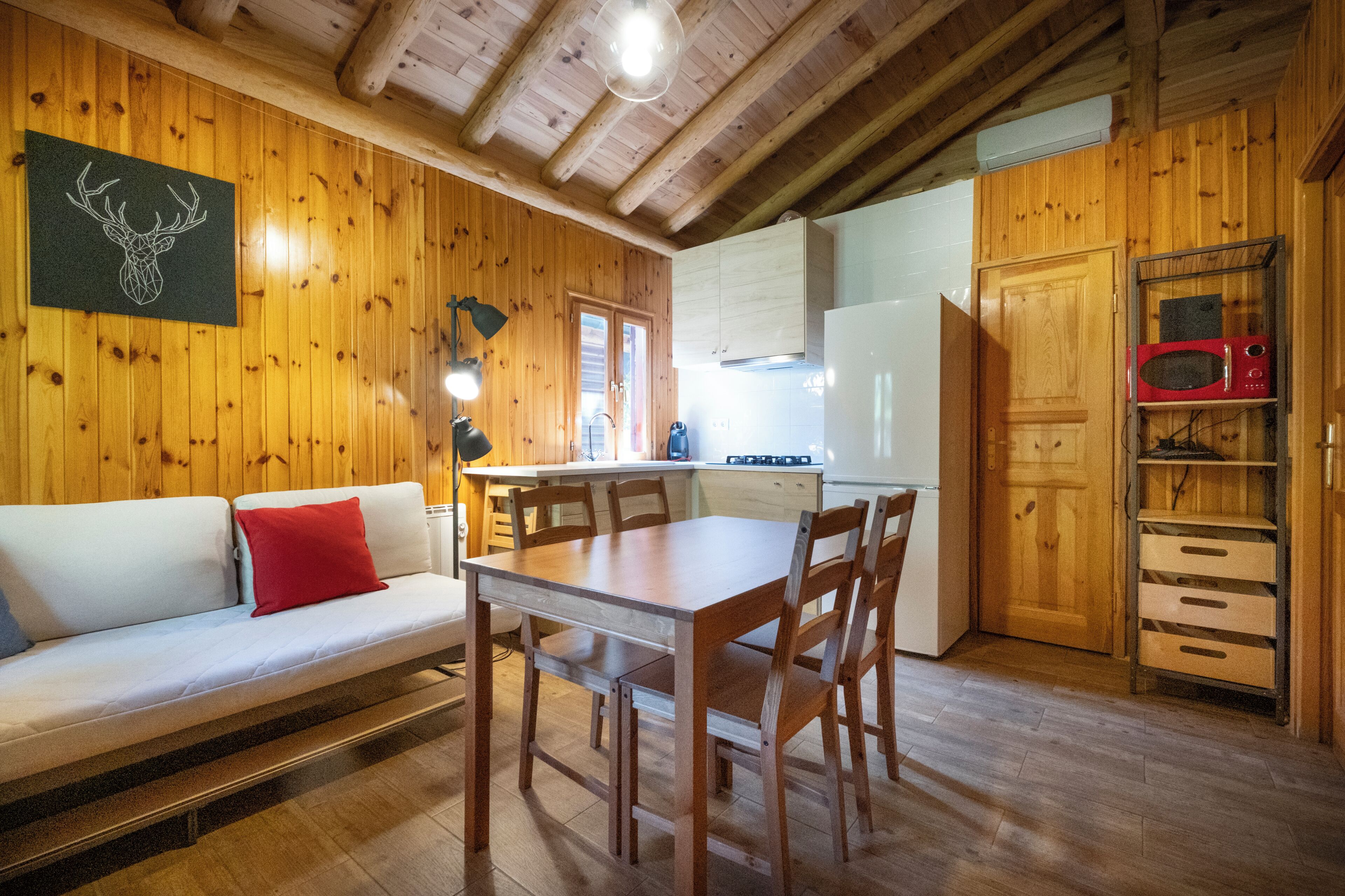 A wooden interior with a sofa, dining table, chairs, a kitchen area, and a microwave.