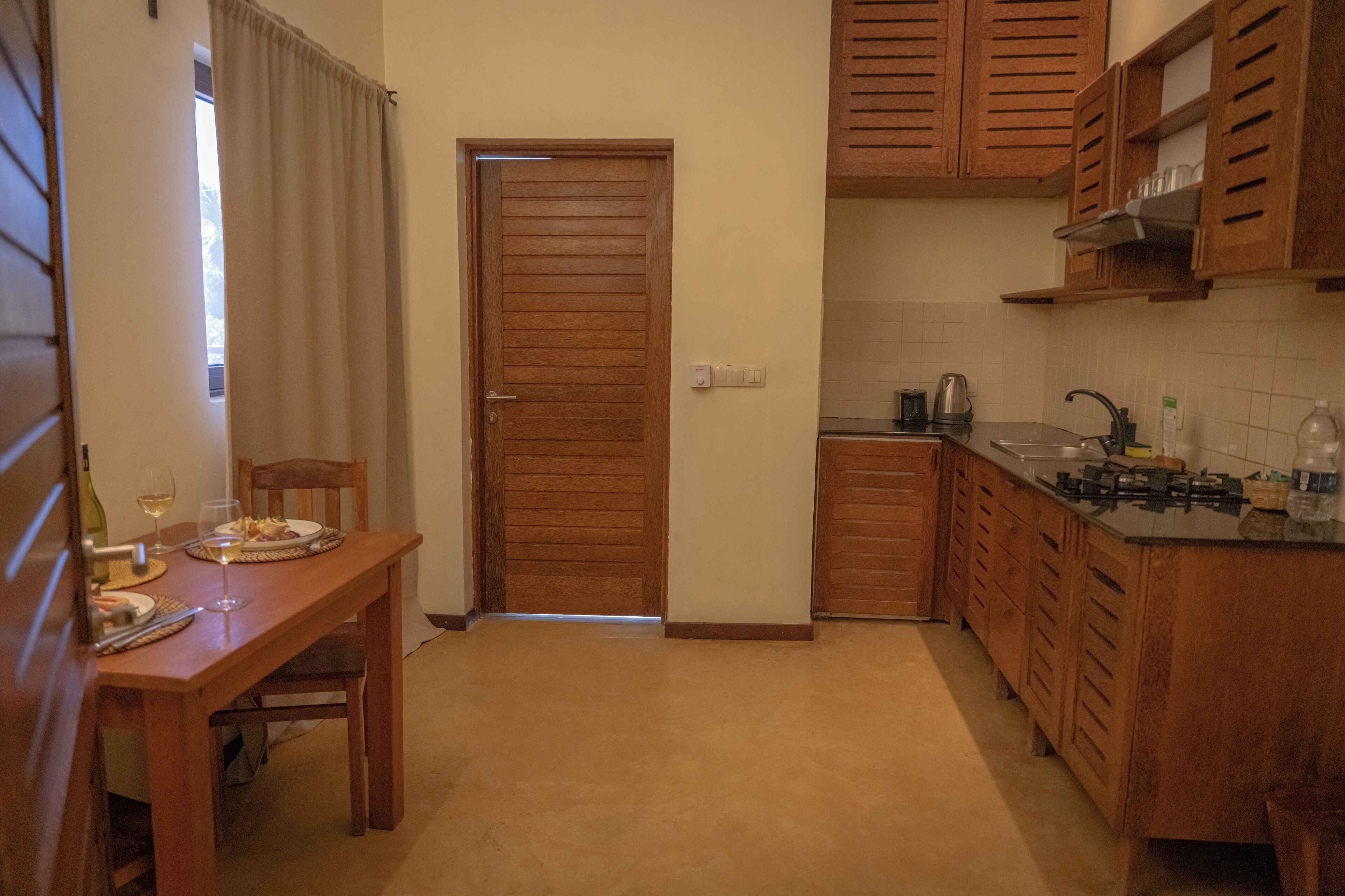 Une cuisine de taille réduite, dotée de meubles en bois, une table à manger avec des chaises et une porte donnant sur une autre pièce.