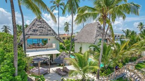 Un resort con edificios de techo de paja, piscina y exuberante vegetación tropical.