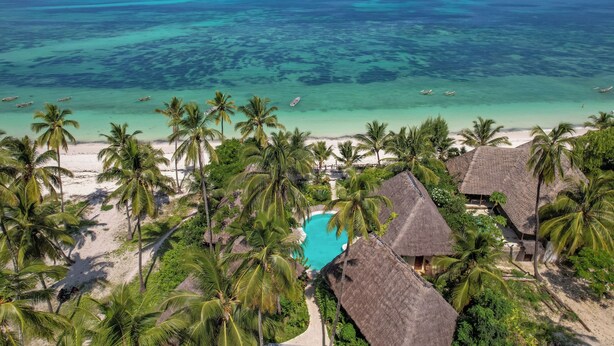 Un resort tropical con un mar turquesa cristalino, palmeras y cabañas de techo de paja.