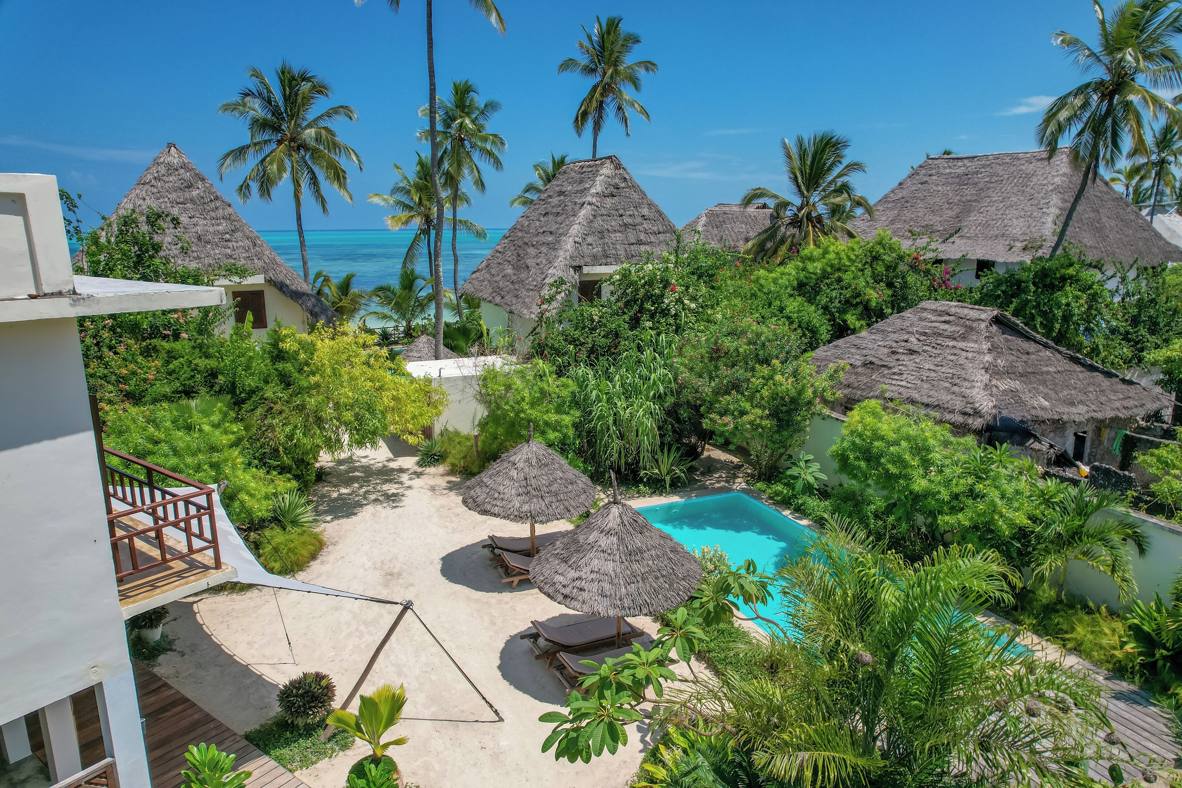 Ein Resort mit strohgedeckten Hütten, einem Swimmingpool und üppiger Vegetation.