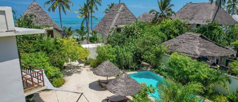 Ein Resort mit strohgedeckten Hütten, einem Swimmingpool und üppiger Vegetation.