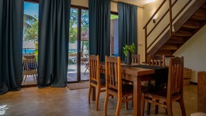Un comedor con una mesa y sillas de madera, una escalera y ventanas amplias con cortinas.