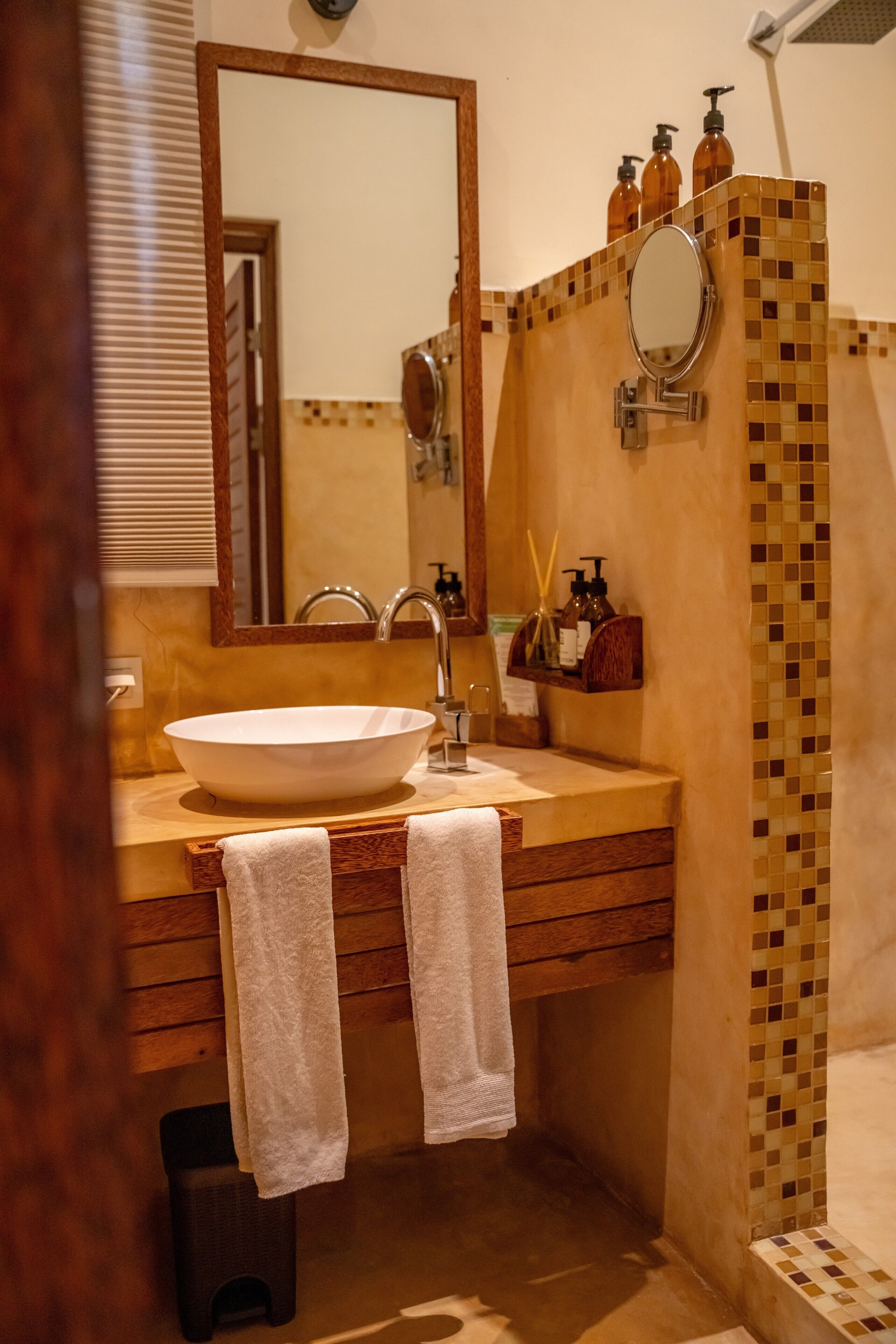 Une salle de bain dotée d’un grand lavabo ovale, d’un miroir et d’un espace douche aux carreaux en mosaïque.