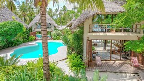 Un resort con piscina, construcciones de techo de paja y abundante follaje.