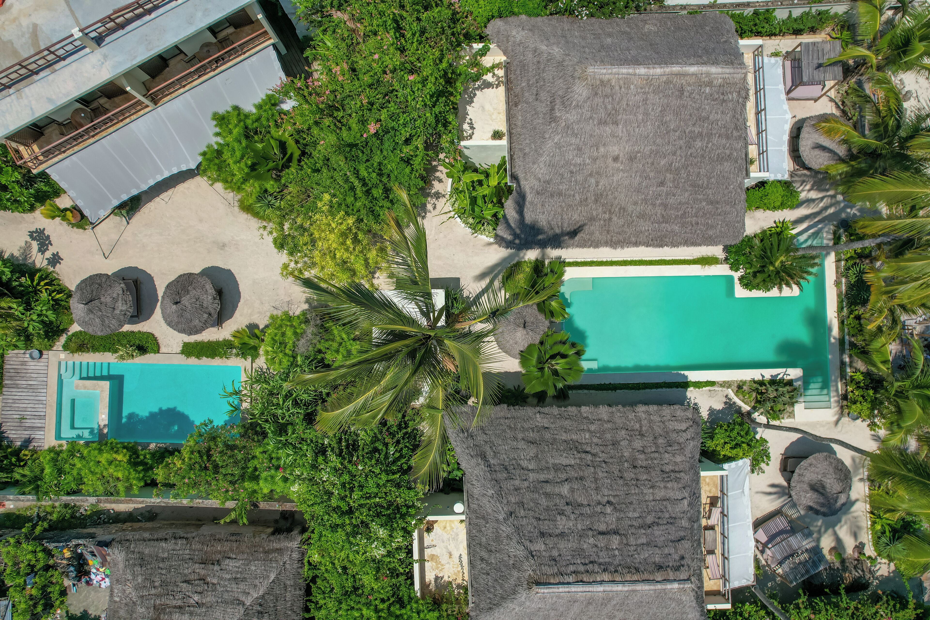 An aerial view of a resort with a swimming pool, thatched-roof structures, and lush greenery.