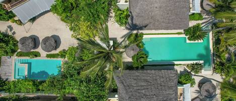 An aerial view of a resort with a swimming pool, thatched-roof structures, and lush greenery.