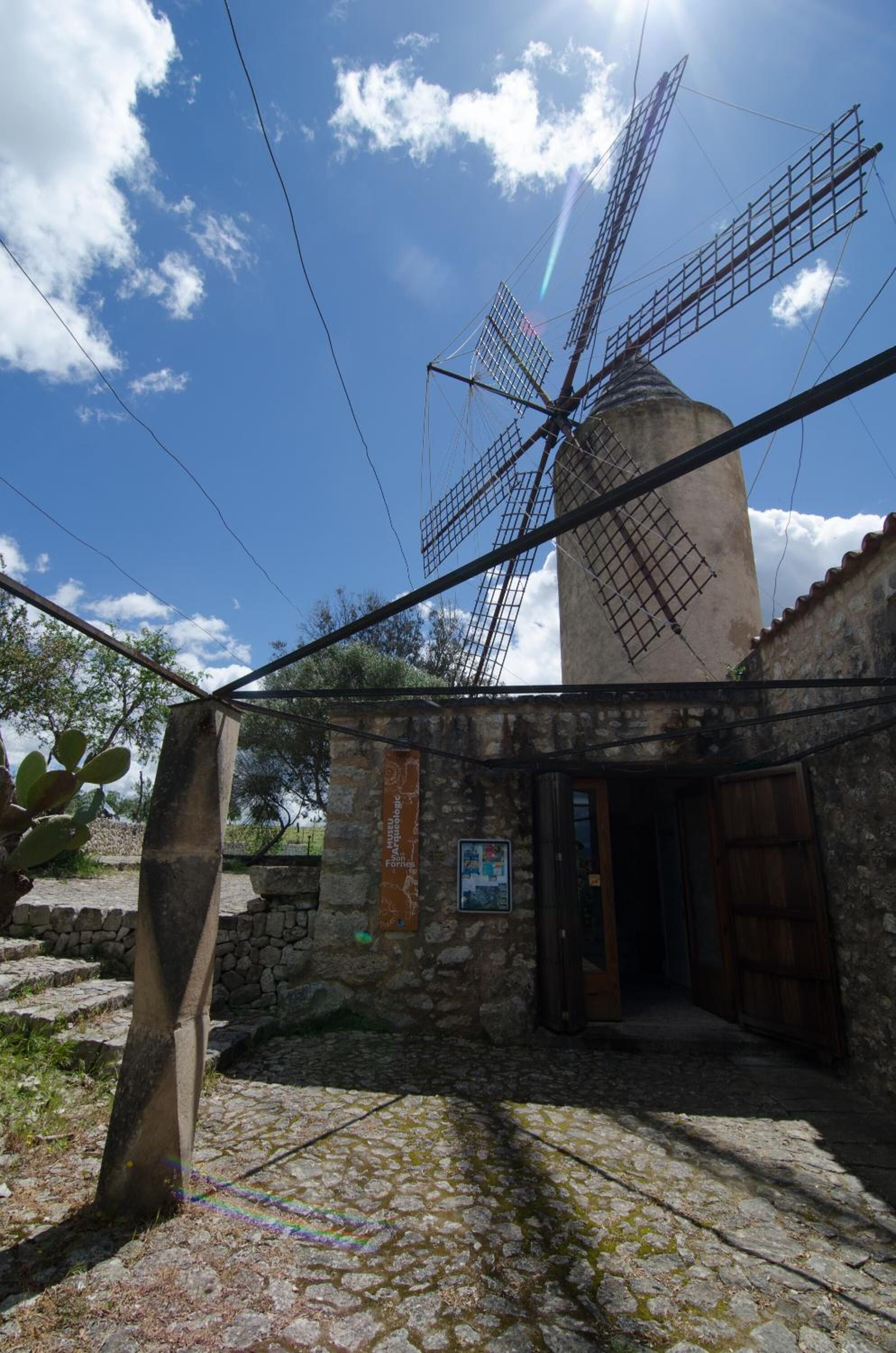 Un moulin à vent doté d’une base en pierre et d’une porte en bois, se dressant sur un ciel bleu dégagé.
