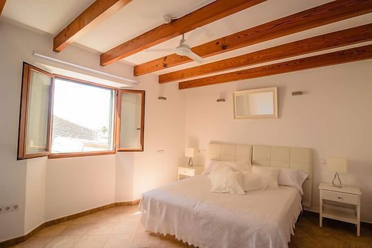 Un dormitorio con una cama grande, vigas de madera, un ventilador de techo y una ventana con vistas.