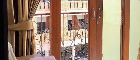 A room with a wooden door leading to a balcony, a wicker basket with towels, and a view of a building with balconies.