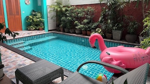 A swimming pool with a pink flamingo float, surrounded by potted plants and wicker furniture.