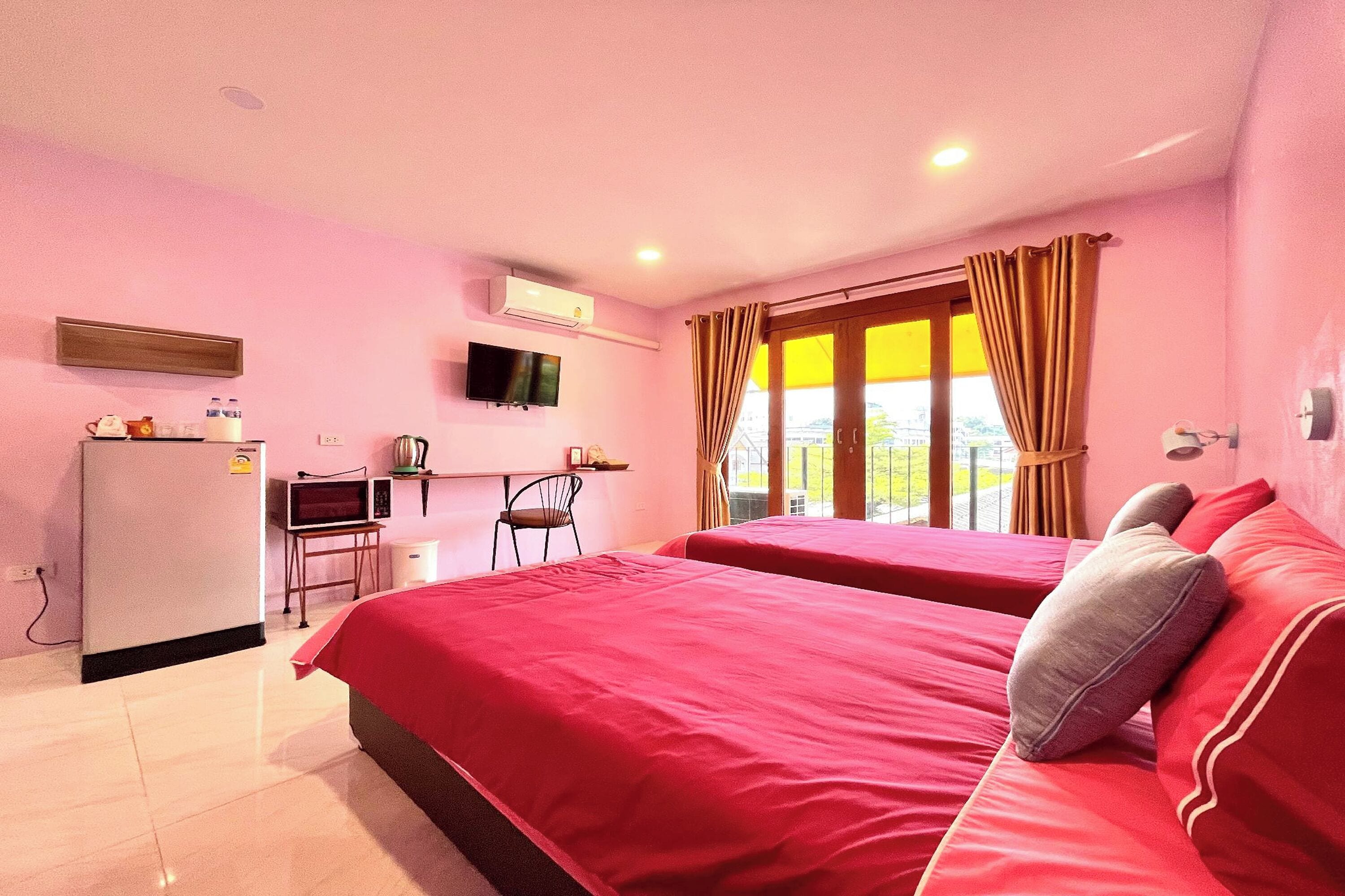 A hotel room with two beds, a desk with a chair, a TV, and an air conditioning unit.