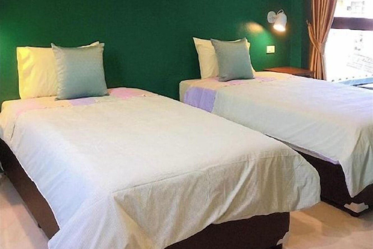 Une chambre avec deux lits, un mur vert et une fenêtre avec des rideaux.