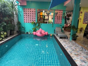 A swimming pool with a pink floatation device, surrounded by potted plants and a tiled floor. - Chor Chang House Chiang Mai (Chiang Mai)