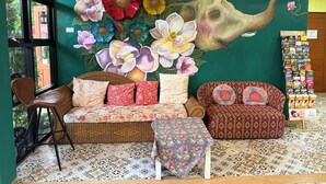 A room with a large floral mural, a wicker sofa, patterned cushions, and a small table.