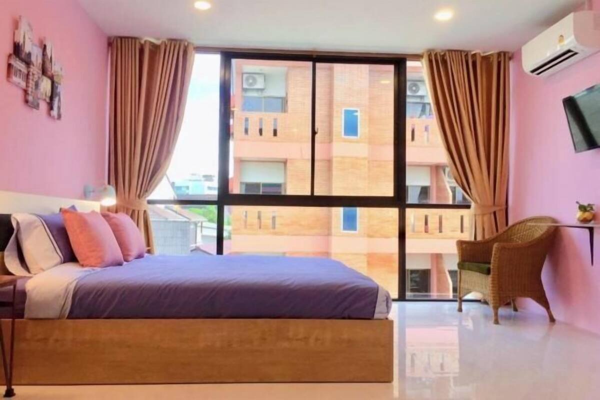 Une chambre avec un grand lit, une chaise, une télévision et une fenêtre avec des rideaux.