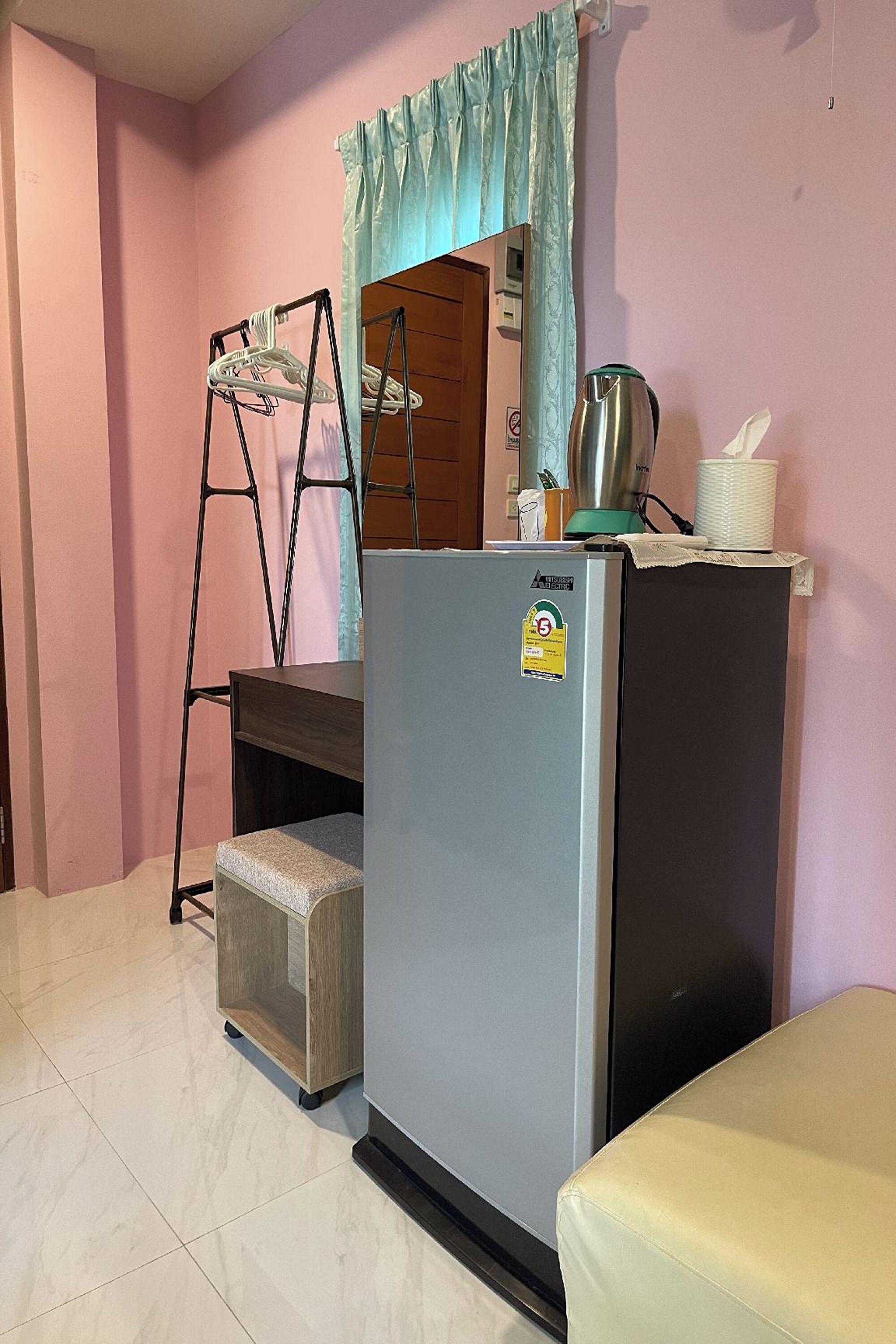 A compact room with a refrigerator, a small wooden cabinet, a metal ladder, and a beige sofa.