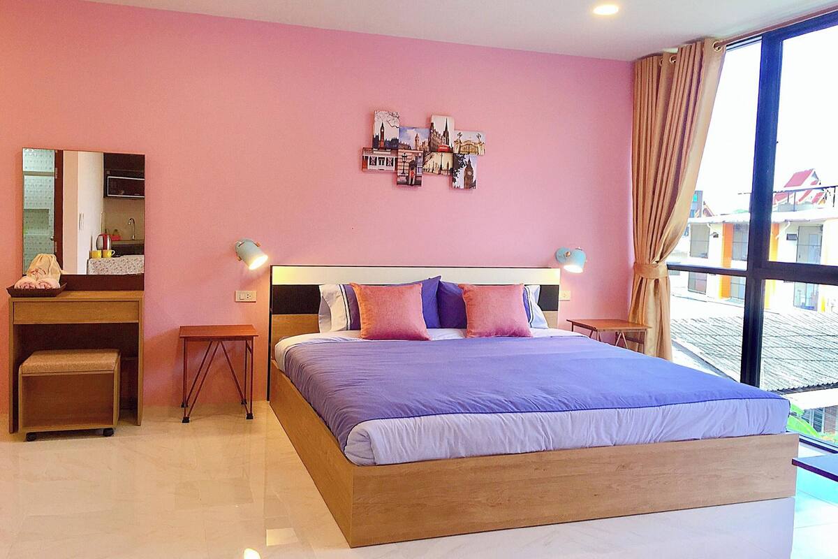 Une chambre avec un grand lit, des tables de chevet, un miroir et une œuvre d’art représentant un paysage urbain accrochée au mur.