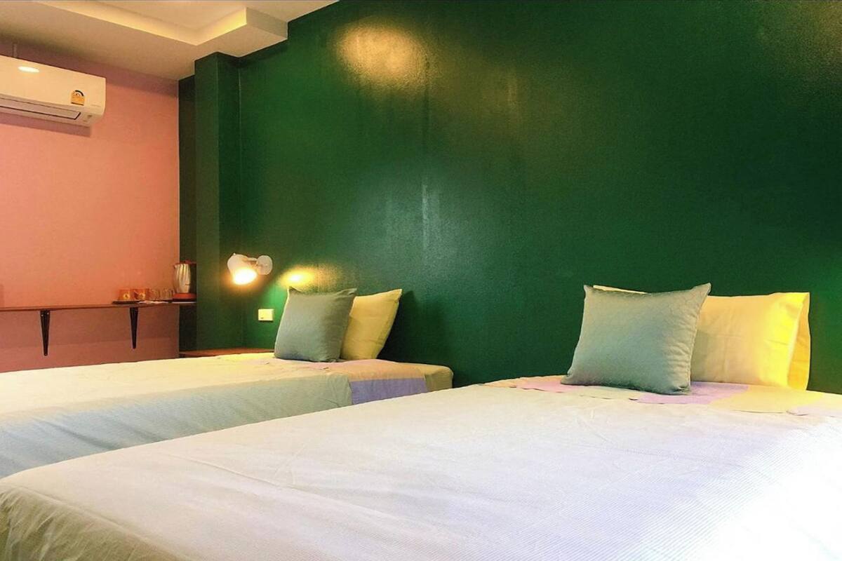 Une chambre d’hôtel avec deux lits, un mur d’accent vert, un petit bureau avec une lampe et un appareil de climatisation.