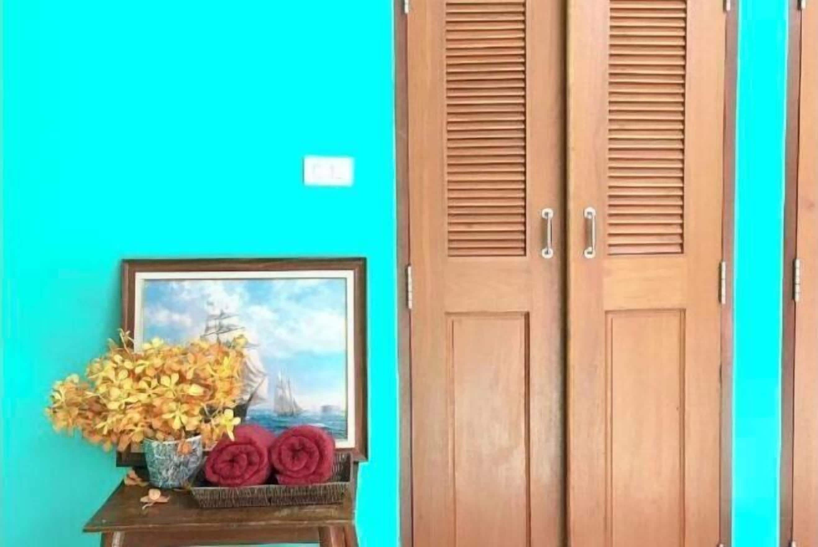 A turquoise wall with a framed picture of a ship and flowers, and a wooden door with louvered panels.