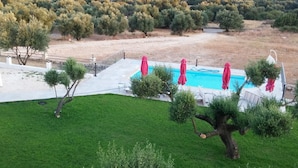 A swimming pool with red umbrellas, surrounded by a grassy area and trees. - Elaias Gi Residence (Kefalonia)