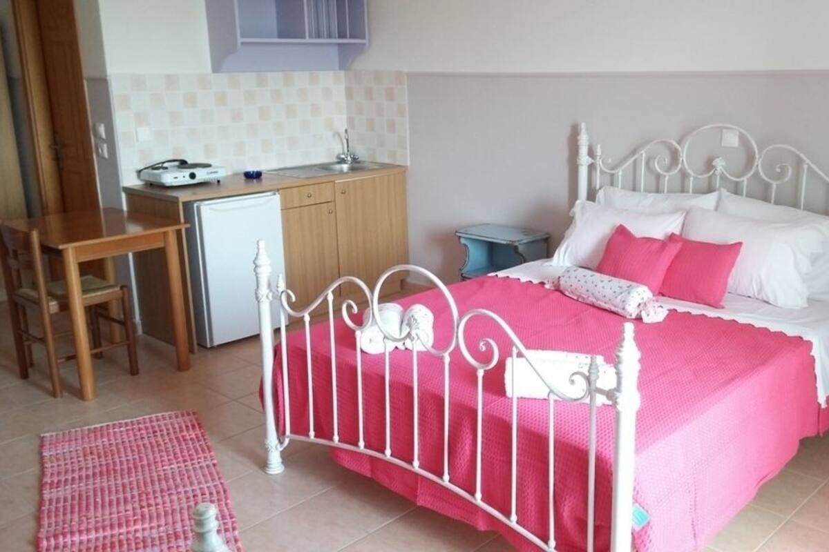 A bedroom with a white metal bed frame, a pink bedspread, and a small desk with a chair.