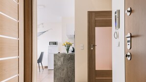 Un pasillo moderno con suelo de madera, una zona de cocina con una isla de hormigón y una puerta con teléfono y cerradura.