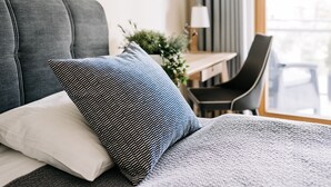 Una cama con cabecera gris, almohada blanca y una almohada con estampado azul y blanco.