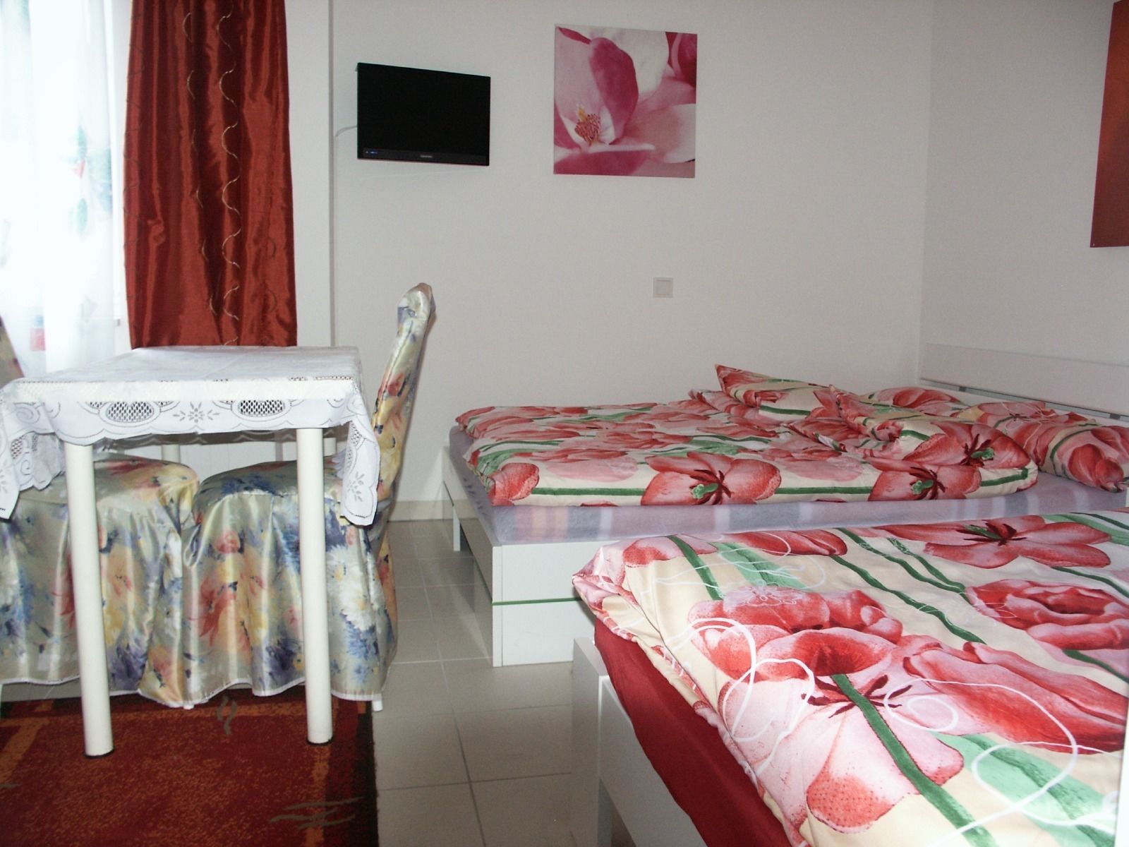 A bedroom with a bed, a chair, a table, and a TV on the wall.