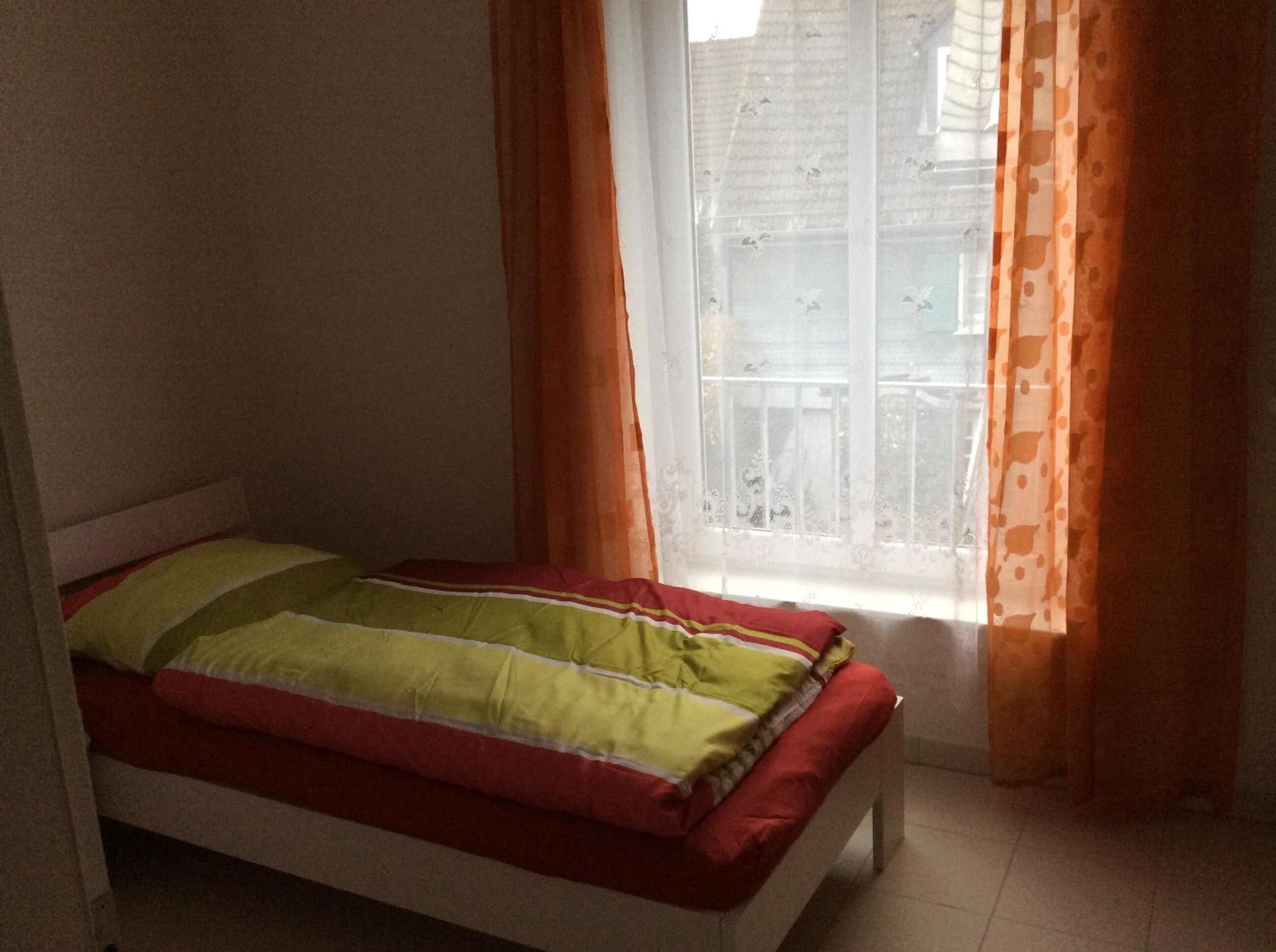 A small, single-bed room with a window and curtains.