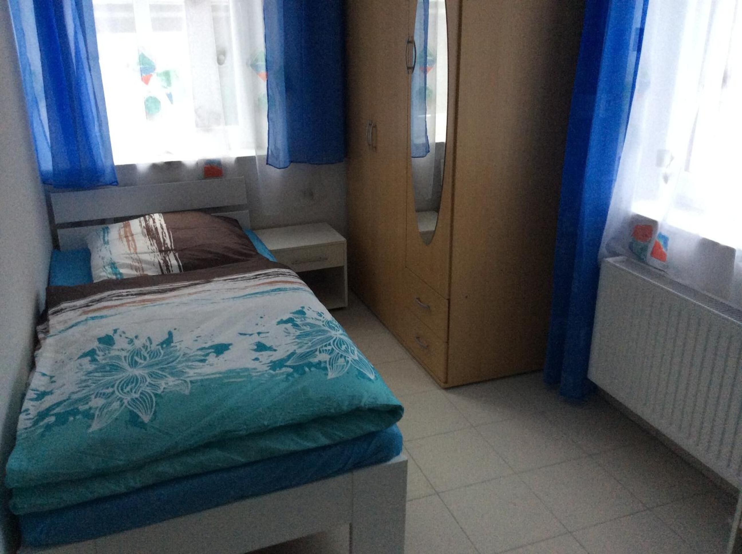 A bedroom with a bed, a nightstand, a wardrobe, and a window with curtains.