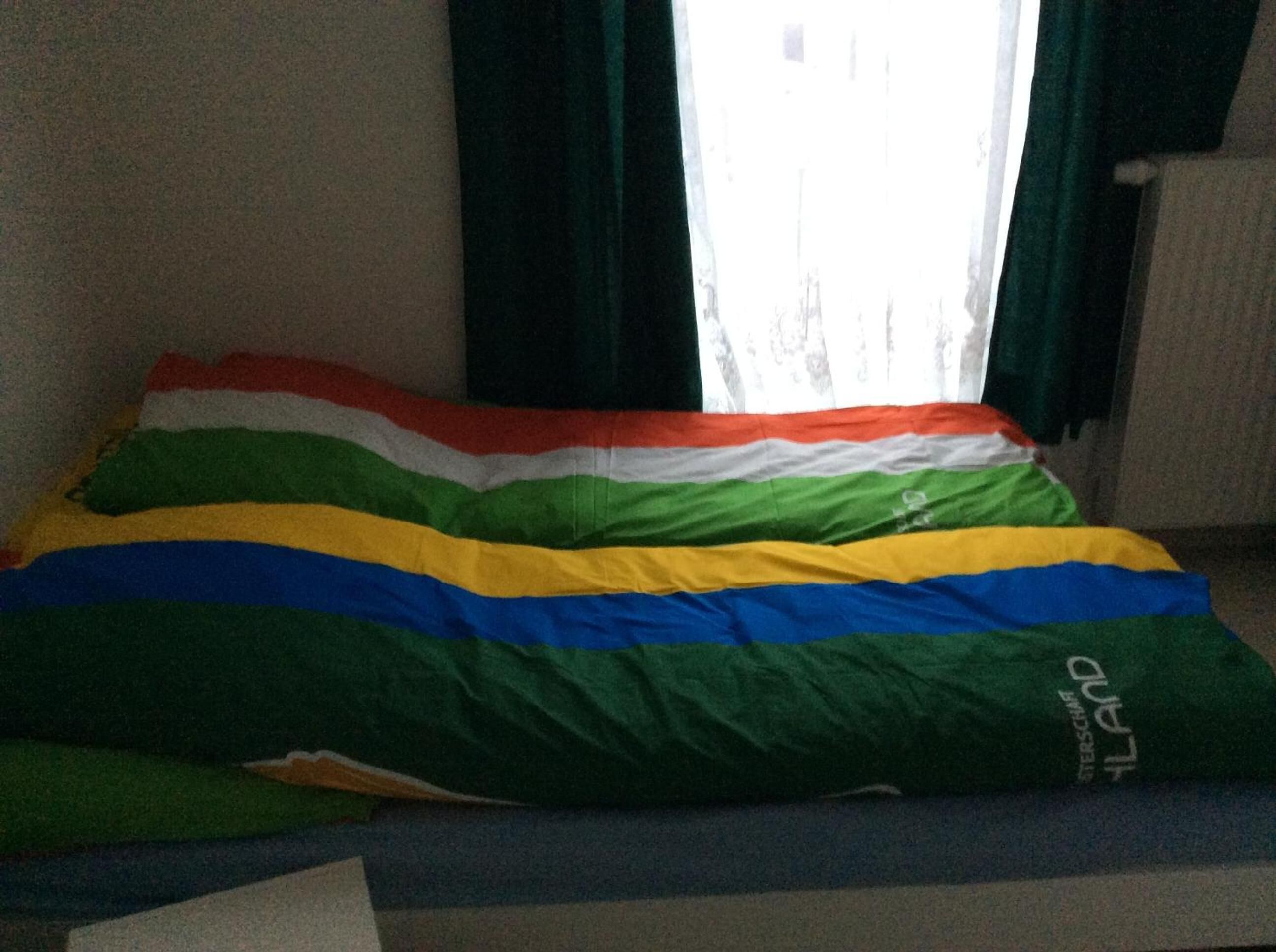 Un lit avec une couverture à rayures arc-en-ciel et un oreiller orné du mot « STERSCHL ».