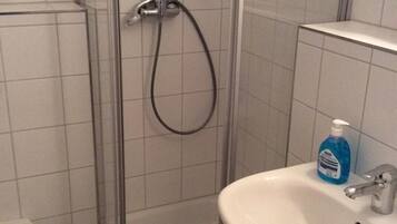 A bathroom with a shower enclosure, a toilet, and a sink with a soap dispenser.