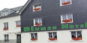 A hotel named Blumen Hotel with a white facade and multiple windows adorned with red flowers. - Blumenhotel (Bergneustadt)