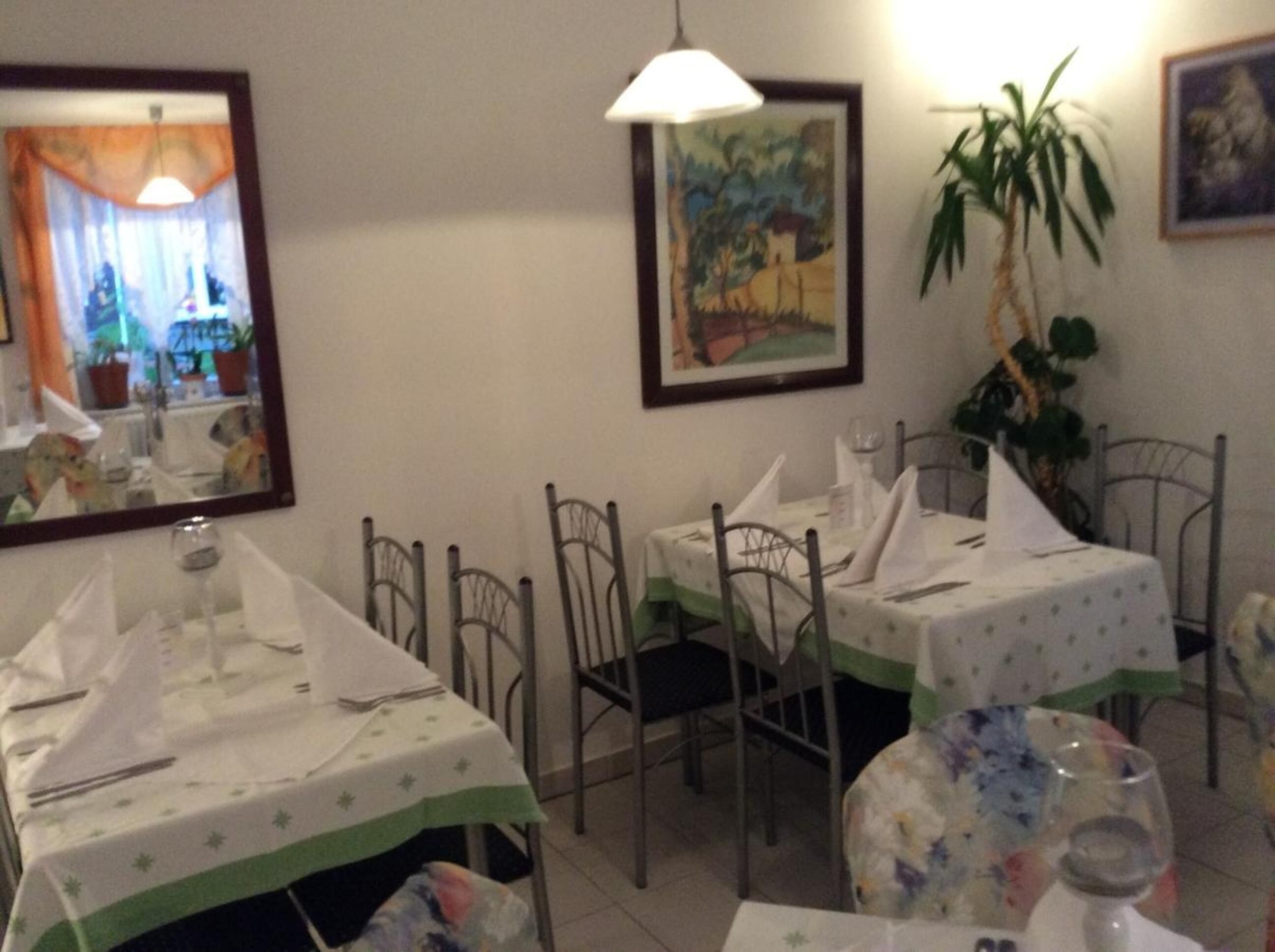 A dining area with tables set for two, chairs, and a painting on the wall.