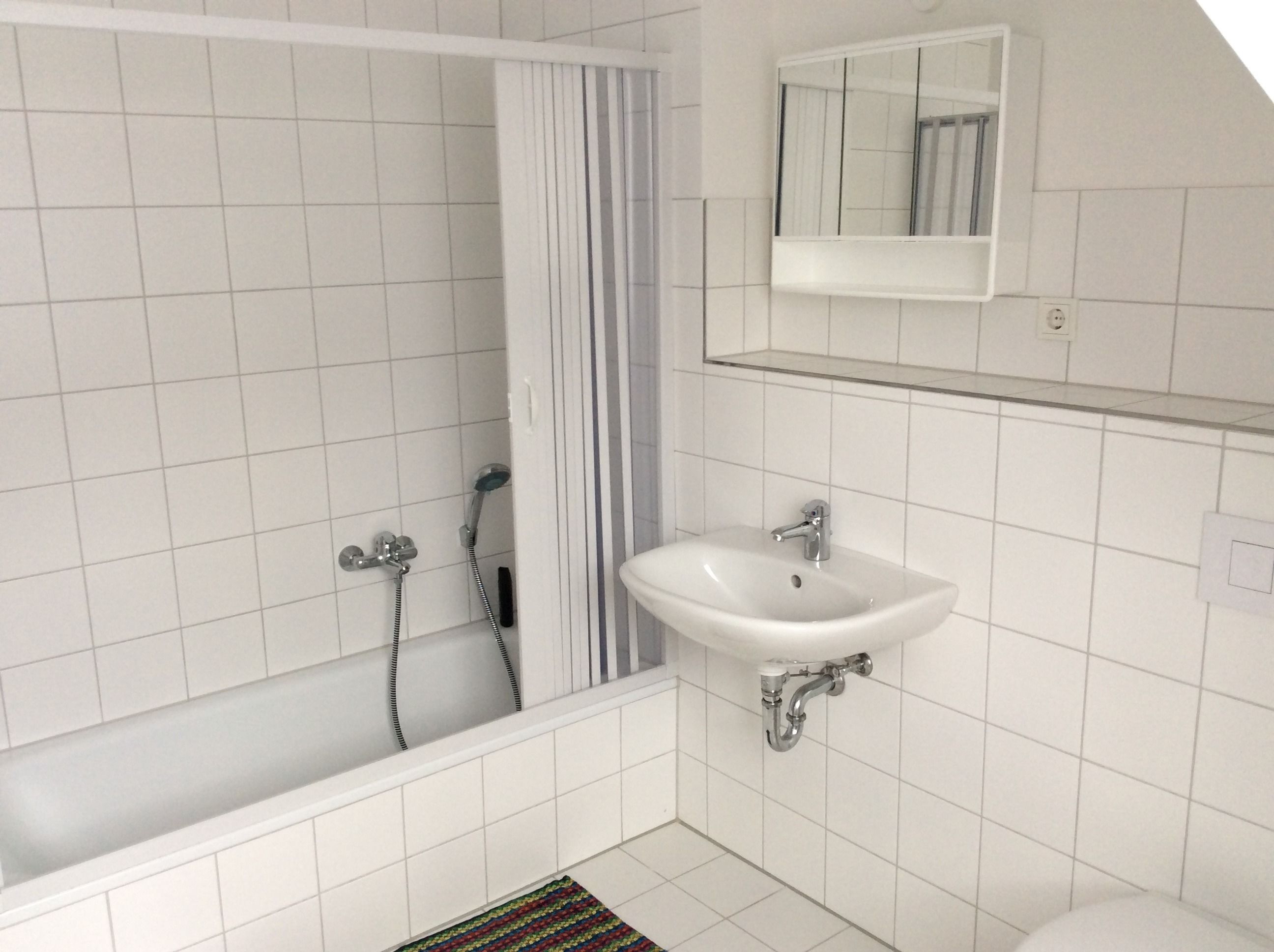 Un baño con azulejos blancos, una bañera, un lavabo y un espejo.