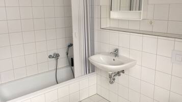 Un baño con azulejos blancos, una bañera, un lavabo y un espejo.