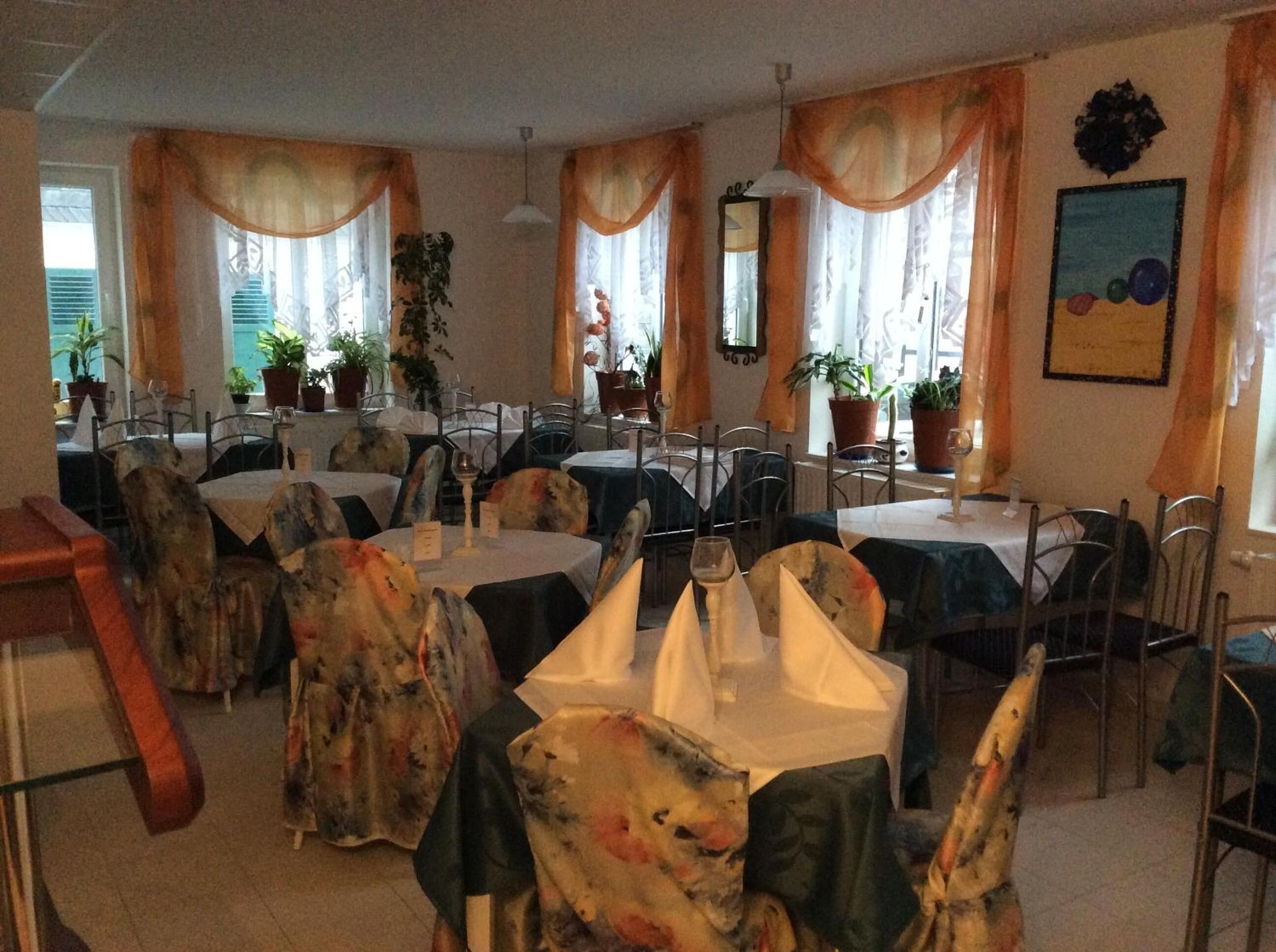 A restaurant with round tables, chairs, and potted plants.